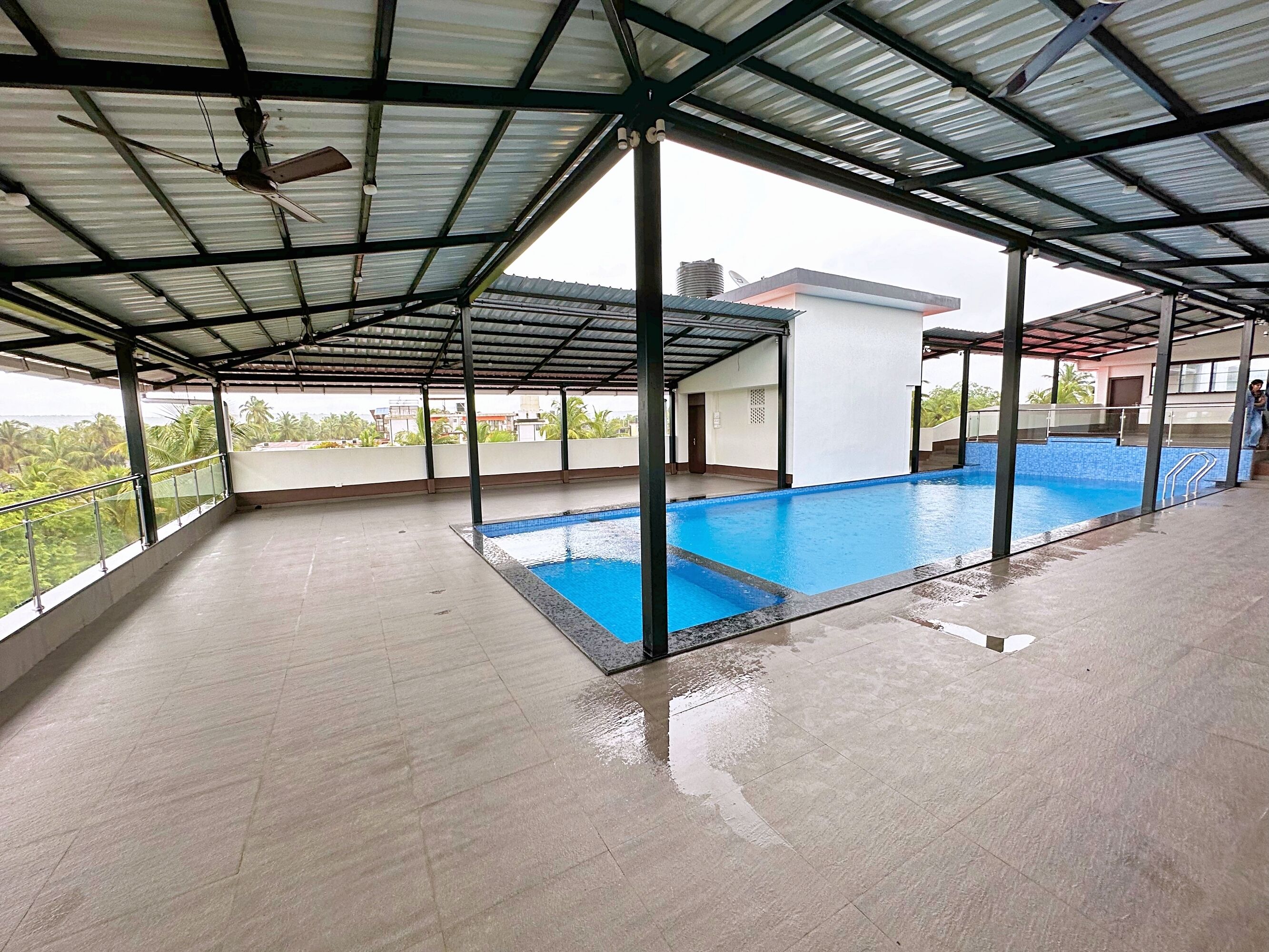 A covered swimming pool with a metal roof, surrounded by a tiled deck.