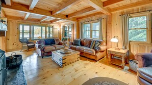 A cozy wooden cabin interior with a fireplace, leather sofas, and large windows. - Lakefront Westhampton Cabin w/ Beach + Kayaks! (Westhampton)