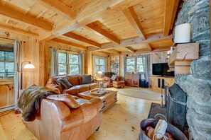 A cozy cabin interior with a large leather sofa, a fireplace, and a stone wall.