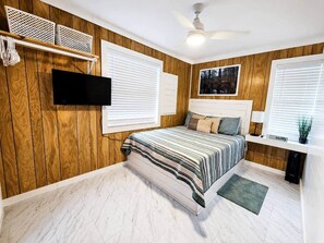 Une chambre à coucher avec un lit, des murs recouverts de panneaux en bois, un ventilateur de plafond et un téléviseur fixé au mur.