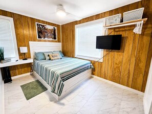 Une chambre à coucher avec un lit, un téléviseur fixé au mur, un lambris en bois et une fenêtre avec des stores.