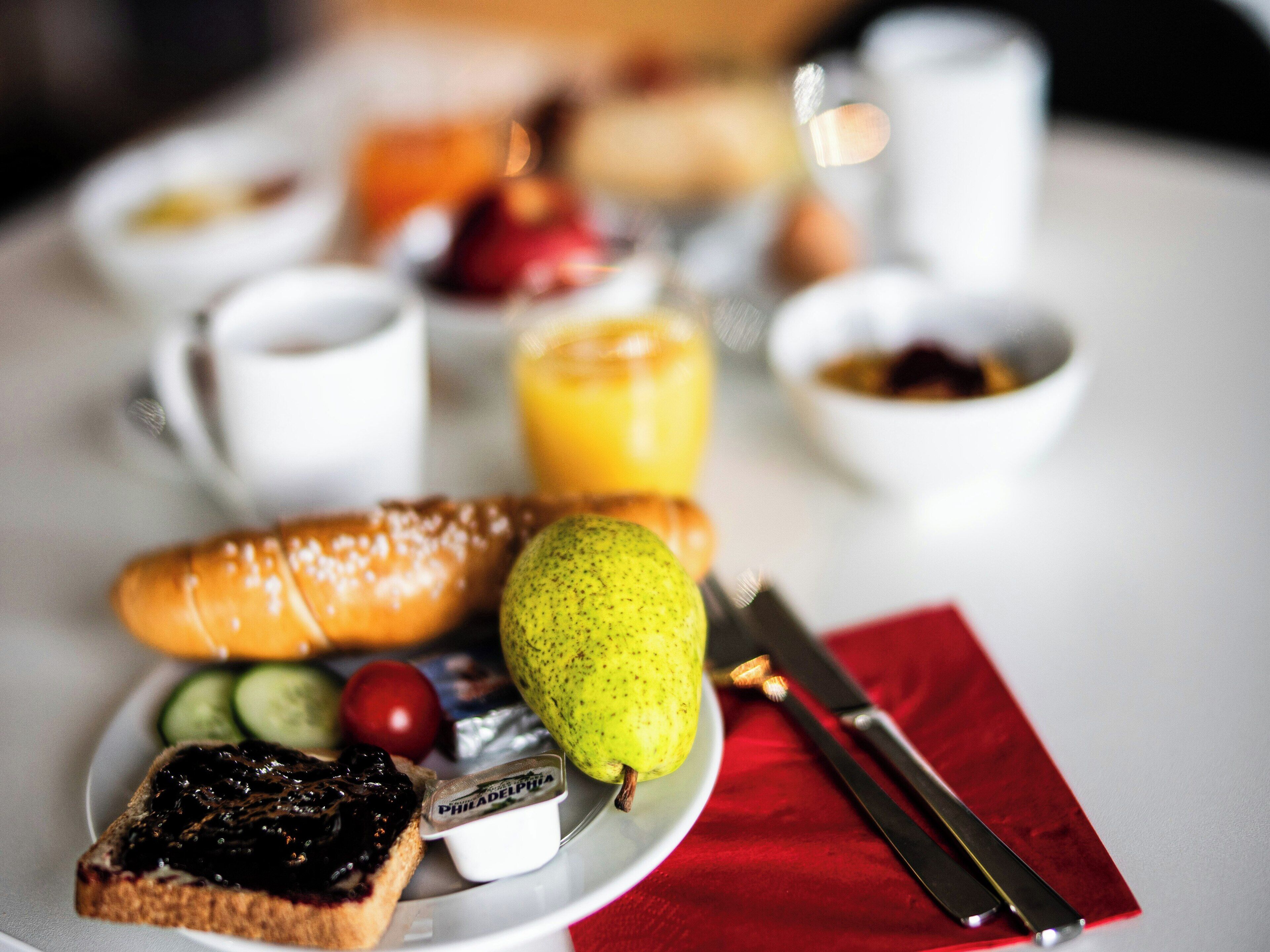 A breakfast plate with toast, a pear, a small container of jam, a slice of cheese, and a cup of orange juice.