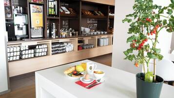 Ein Café mit einer weißen Theke, einer Kaffeemaschine und einem Blumentopf mit Tomaten.