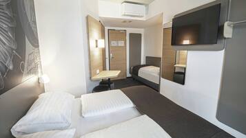 Habitación de hotel con dos camas, un escritorio, un televisor de pantalla plana y aire acondicionado instalado en la pared.