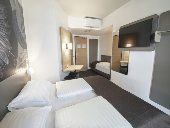 Ein Hotelzimmer mit zwei Betten, einem Schreibtisch, einem Flachbildfernseher und einer Wand-Klimaanlage.