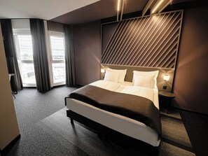 Een moderne hotelkamer met een groot bed, een nachtkastje, een wandlamp en uitzicht door het raam.