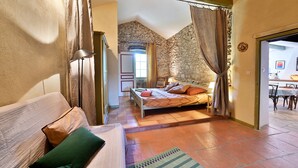 Een slaapkamer met een bed, een bank en een eethoek, zichtbaar door een open deur.