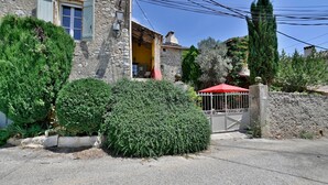 A stone house with a yellow door, a red umbrella, and a gated entrance.