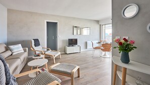 Un salon moderne avec un canapé, des fauteuils, un téléviseur et un vase de fleurs.