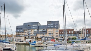 Un port de plaisance avec des bateaux amarrés, un immeuble doté de nombreux balcons et un panneau indiquant « sapeurs-pompiers ».