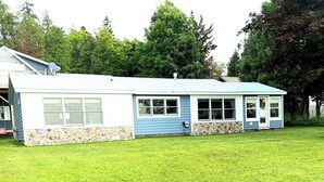A single-story house with a stone foundation and a blue exterior. - Beautiful Huron Bay sunsets from your own private beach. (Skanee)