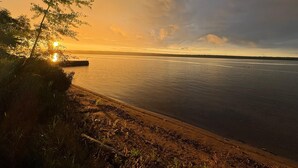 A sunset view over a calm body of water with a dock and shoreline vegetation. - Beautiful Huron Bay sunsets from your own private beach. (Skanee)