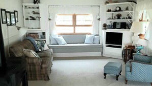 A cozy living room with a fireplace, a sofa, a blue armchair, and a built-in bench with cushions. - Beautiful Huron Bay sunsets from your own private beach. (Skanee)