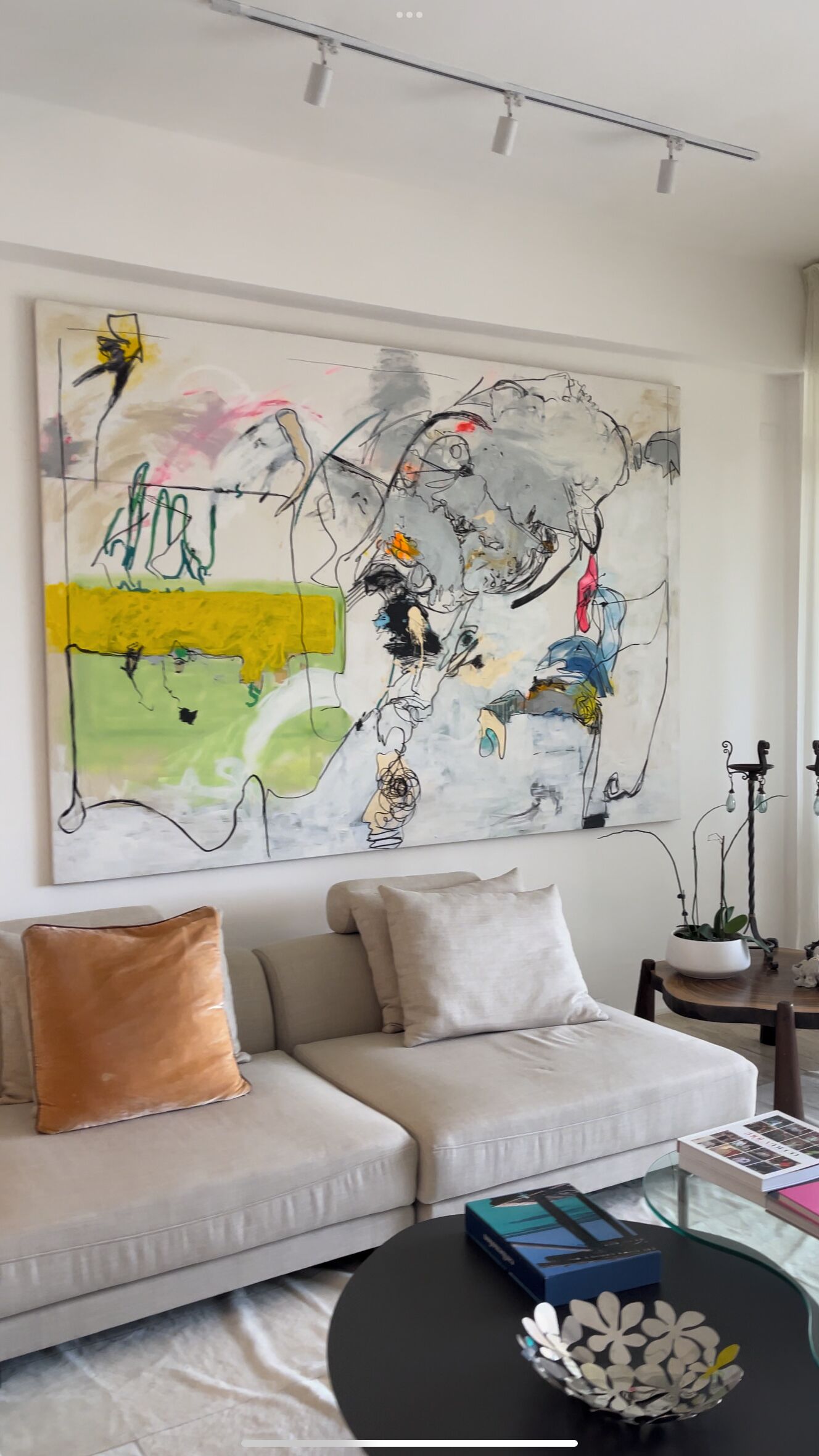 A modern living room with a large abstract painting, a beige sofa, and a black coffee table with decorative items.