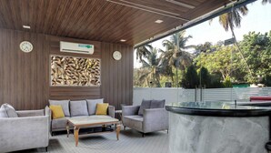 Un área de descanso moderna con sofás, una mesa de centro, un reloj y vistas a palmeras.