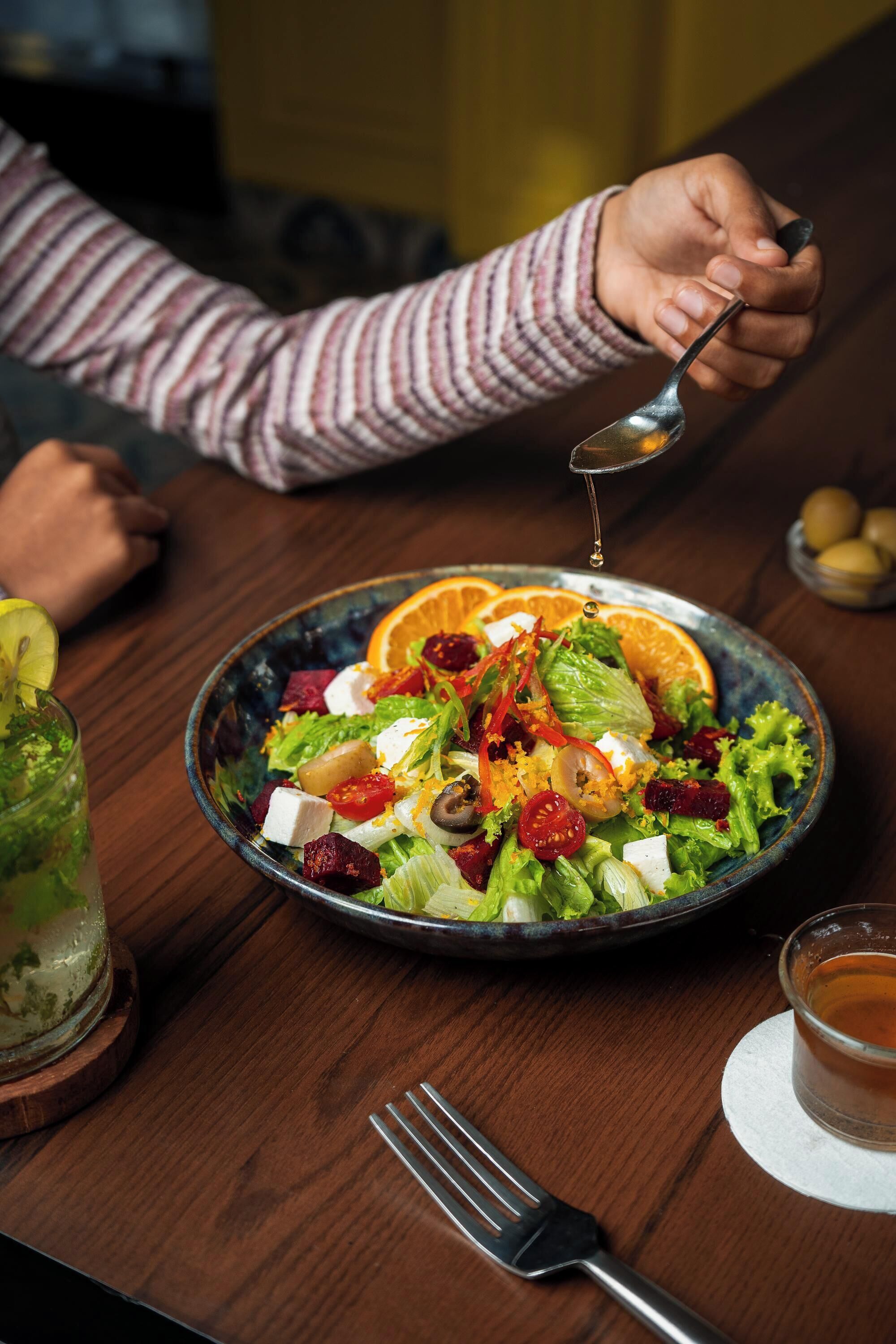 Una mesa con ensalada, un tenedor, una taza de té y una cuchara.