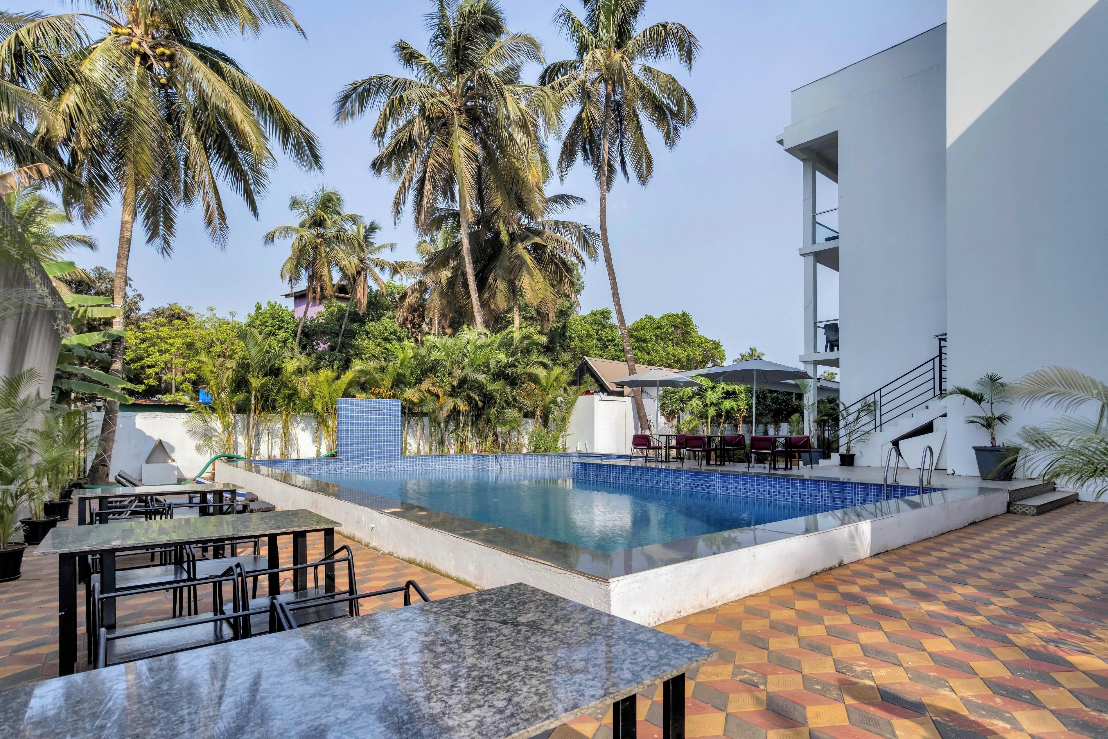 An outdoor swimming pool with a tiled deck, surrounded by palm trees and a modern building.