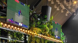 Zona de bar con mostrador, taburetes y una pantalla de televisión mostrando un partido de cricket.