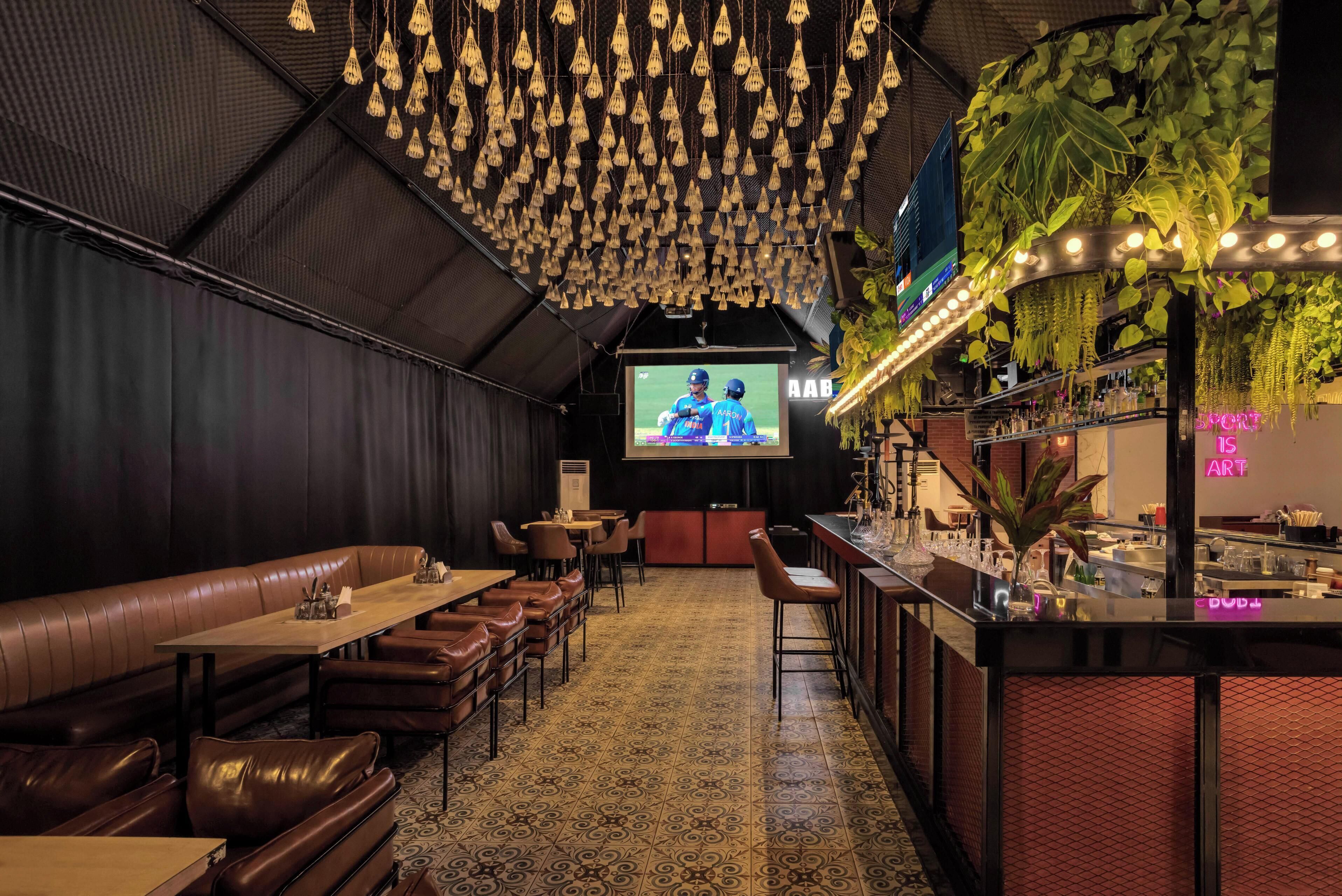 A bar area with a long counter, bar stools, and hanging plants.