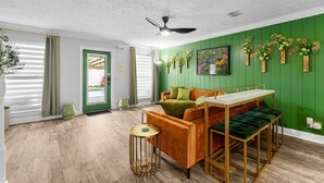 Una habitación con pared verde, suelo de madera, un sofá, una mesa y un ventilador de techo.