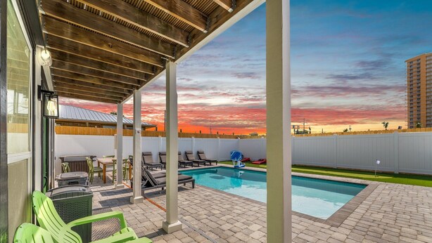 Un espacio al aire libre cubierto con piscina, sillas de descanso y vistas al atardecer.