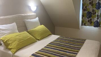 A bedroom with a bed, pillows, a striped blanket, a nightstand, and a wall-mounted lamp.