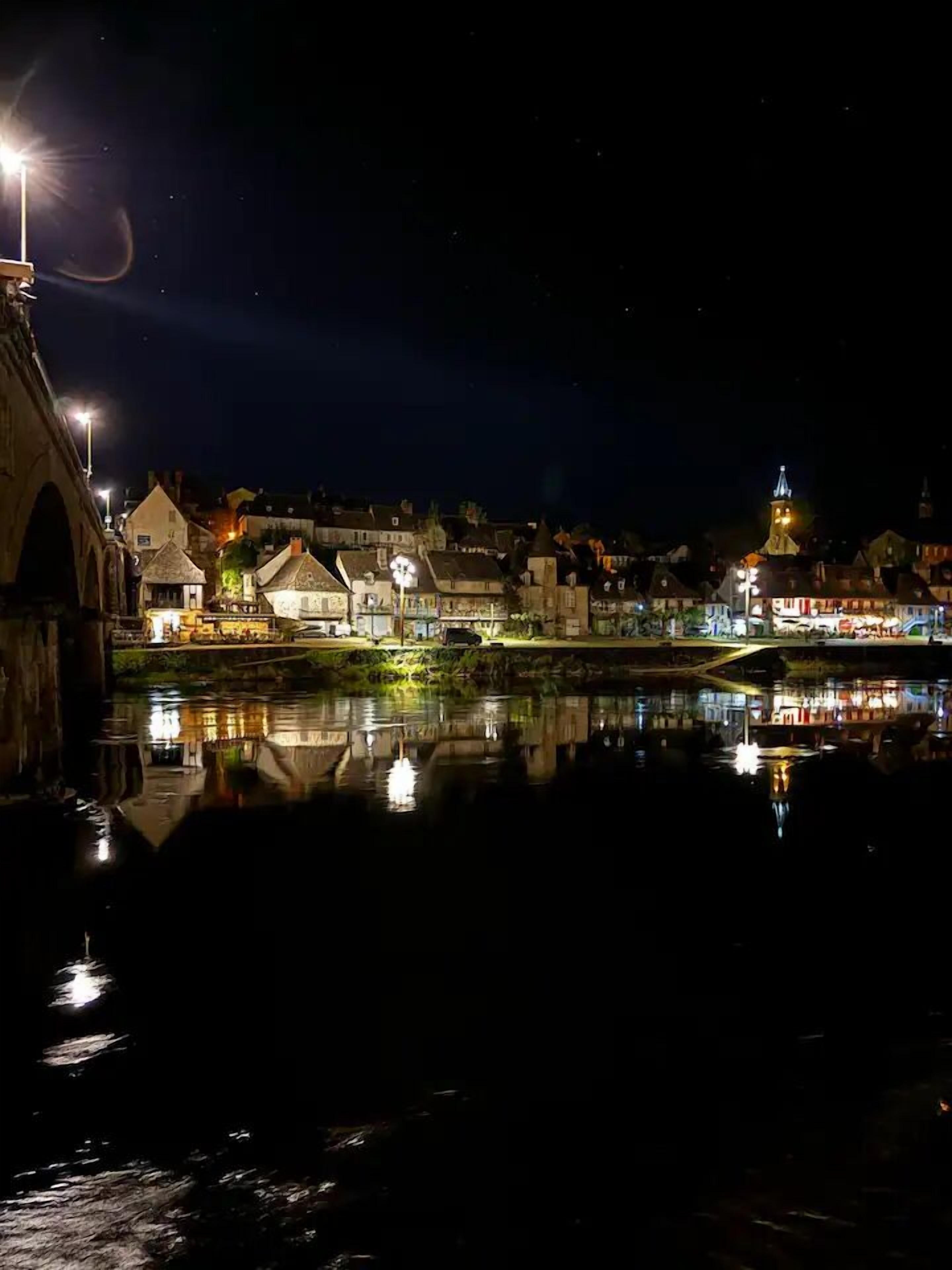 Een nachtzicht van een stad aan de rivier, met verlichte gebouwen en een brug.