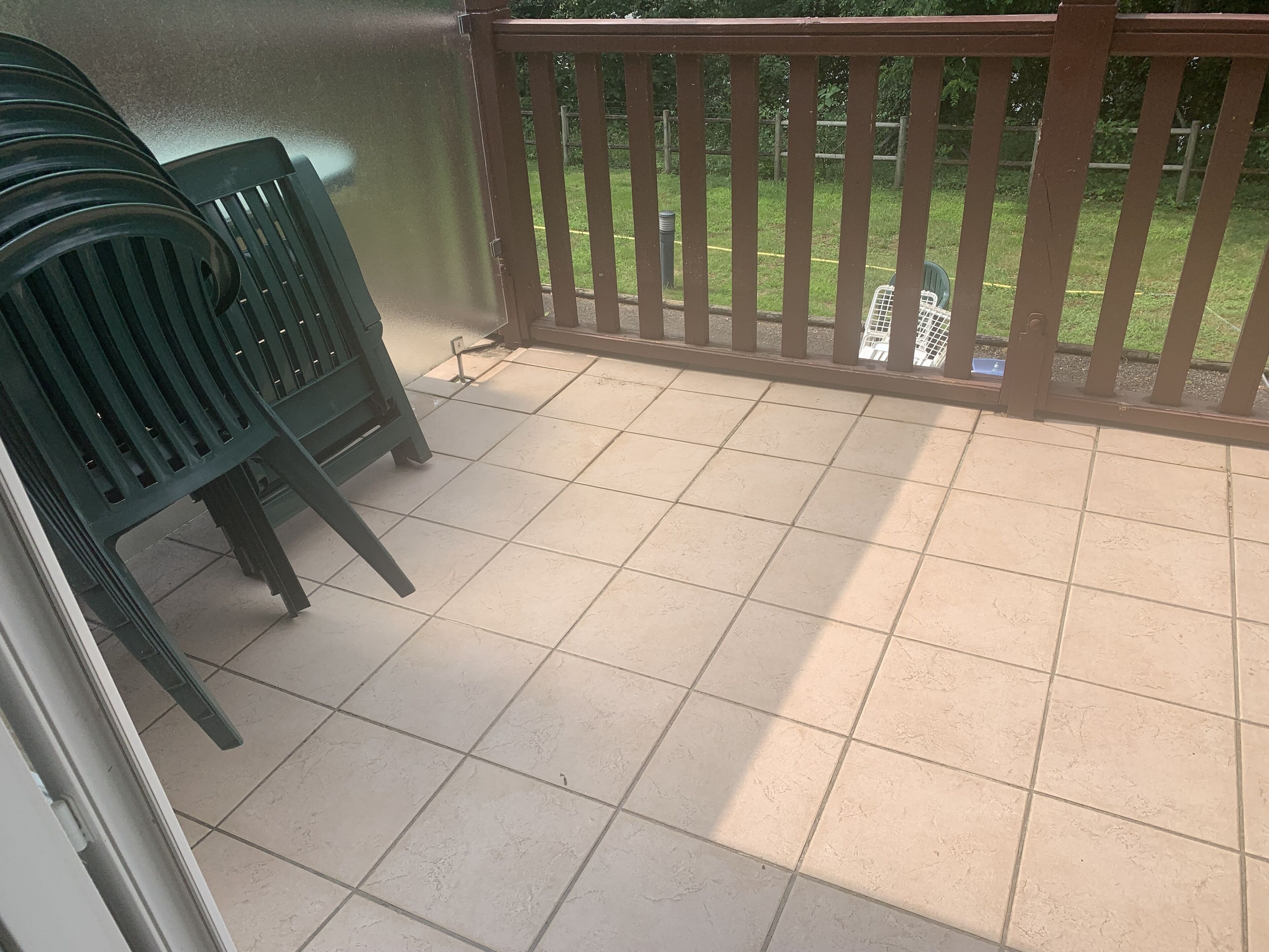 A balcony with tiled flooring, a metal railing, and several green plastic chairs.