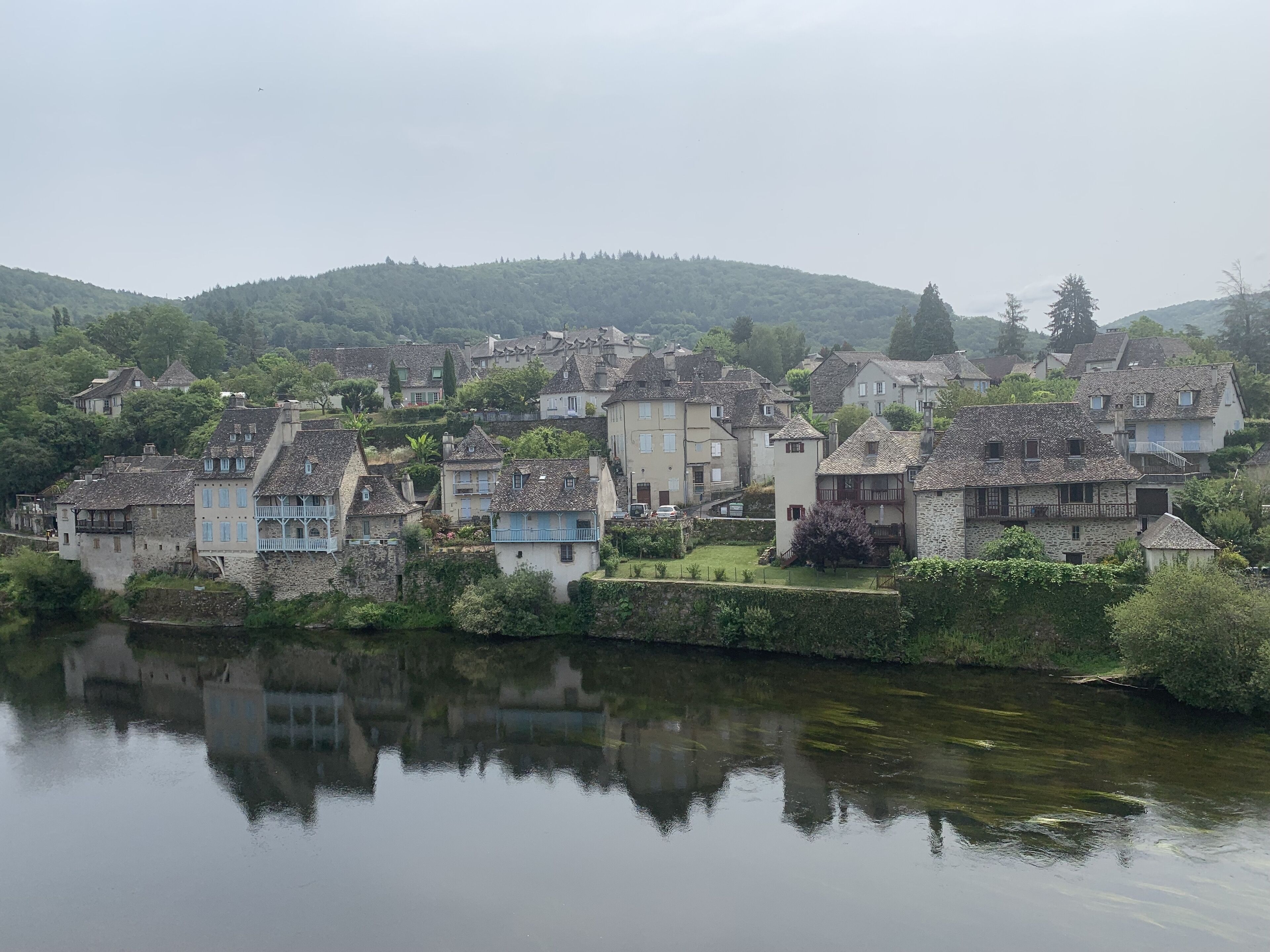 A riverside village with stone buildings, some with balconies, and a calm river reflecting the structures.