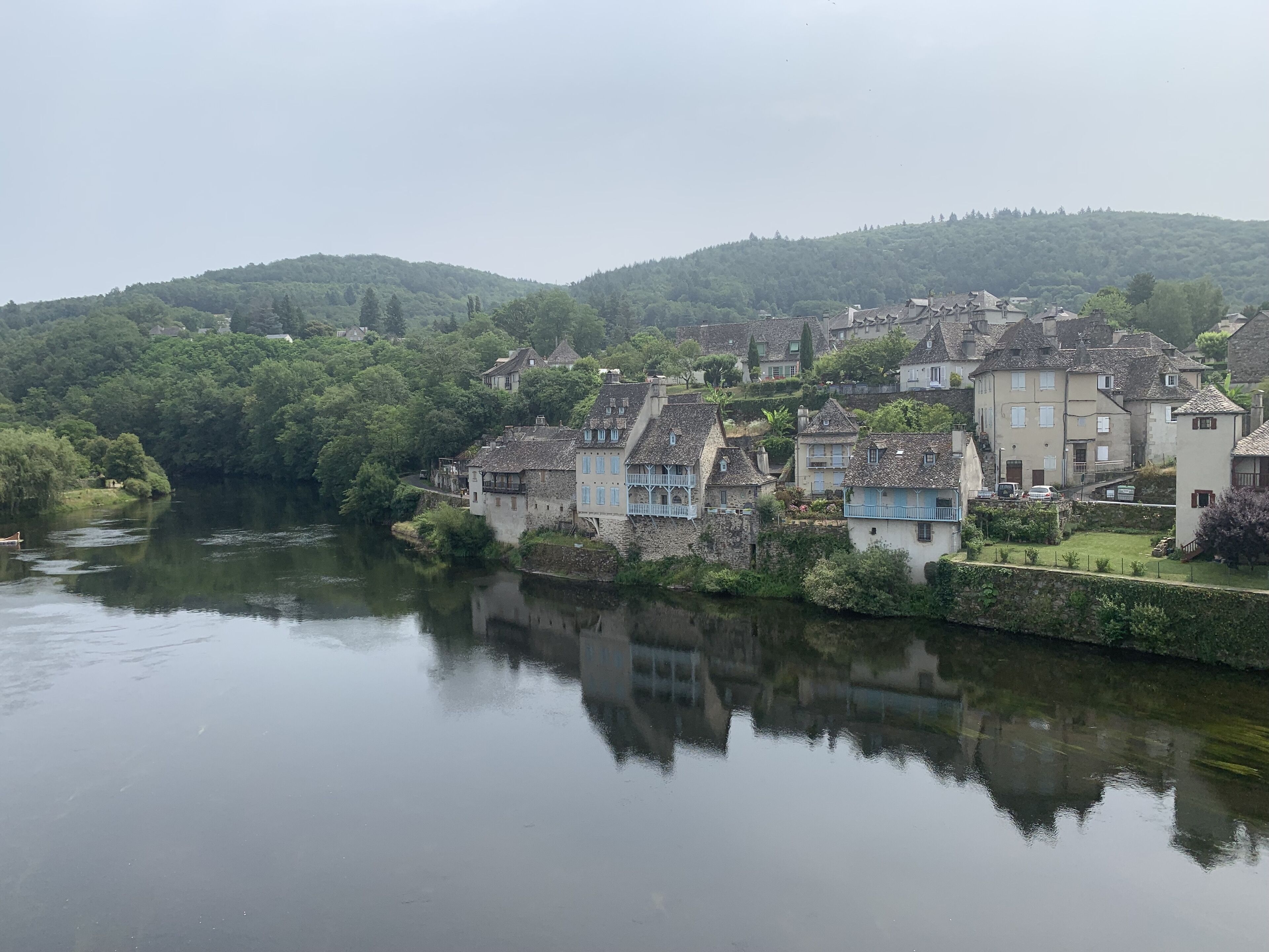 Un pueblo a orillas del río con edificios tradicionales, un río tranquilo y abundante vegetación.