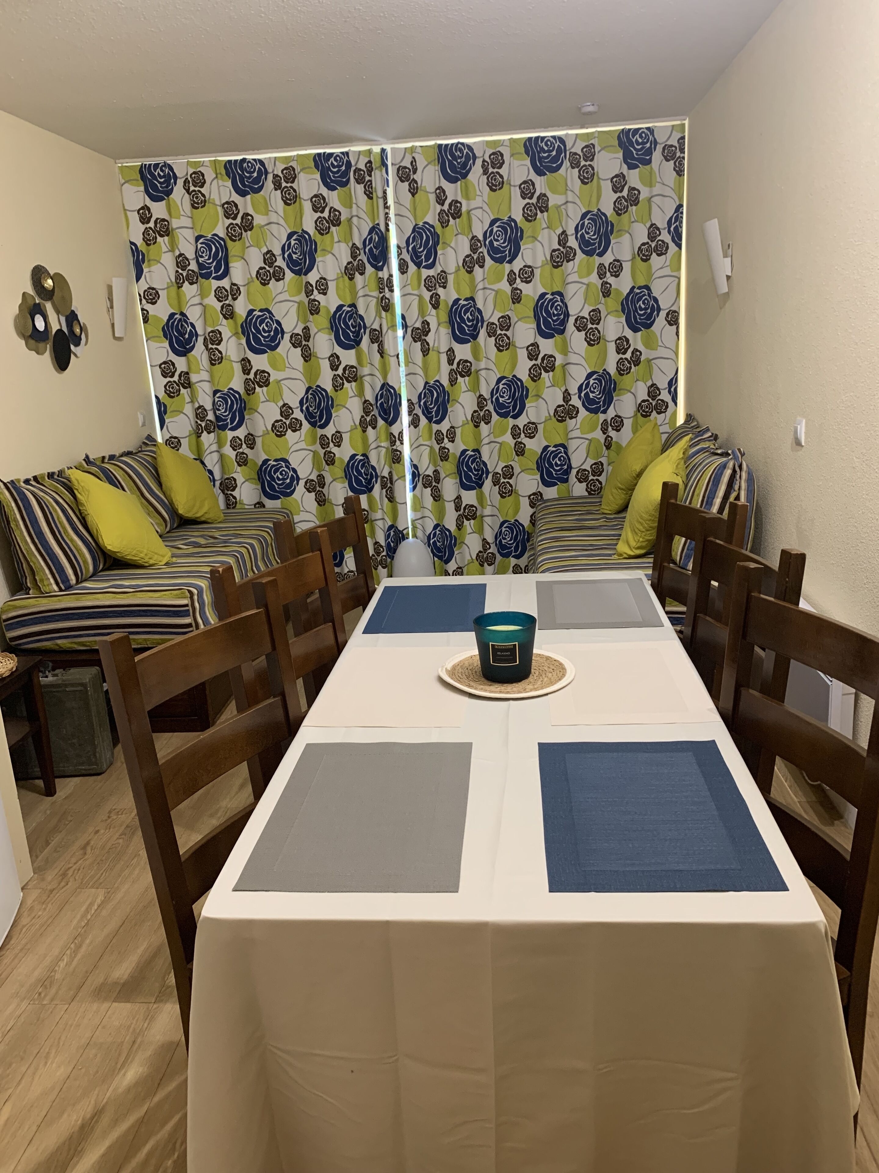 Un coin repas avec une table dressée pour quatre personnes, entourée de chaises en bois. Un rideau à motifs sépare l’espace.