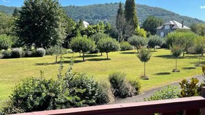 Un jardín ajardinado con diversos árboles y arbustos, un sendero y una casa al fondo.