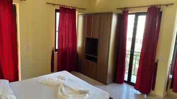 Una habitación de hotel con cama, armario, televisión y cortinas rojas.