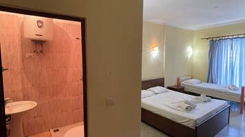 Una habitación de hotel con baño, una cama, una mesita de noche y una ventana con cortinas.