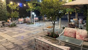 Un patio al aire libre con suelo de baldosas, mobiliario de metal blanco y luces colgantes.