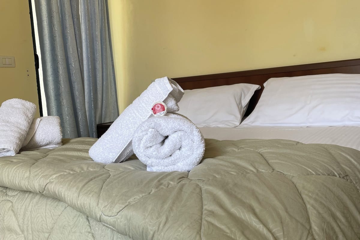 Quarto de hotel com uma cama, um quadro do oceano e uma janela com cortinas.