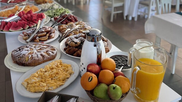 Una mesa de buffet con diversos alimentos para el desayuno, como pasteles, frutas y una cafetera.