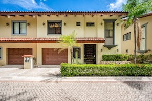A two-story house with a tiled roof, a garage, and a well-maintained front yard with a palm tree and hedges.