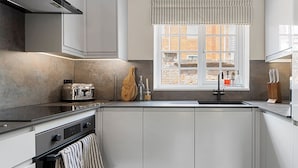 A modern kitchen with white cabinetry, a built-in oven, a stovetop, and a window with a striped valance. - 11 Friernhay Court (Exeter)