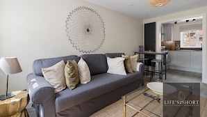 A modern living room with a grey sofa, a glass coffee table, and a decorative wall piece. - 11 Friernhay Court (Exeter)