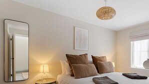 A bedroom with a bed, pillows, a bedside lamp, a mirror, a framed artwork, a window with curtains, and a hanging light fixture. - 11 Friernhay Court (Exeter)
