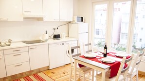 A compact kitchen with white cabinets, a microwave, and a dining area with a red tablecloth. - Apartamento / Estudio no Centro de Lisboa Para Casal ou Família (Lisboa)