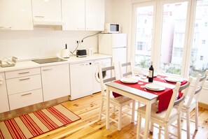 Cozinha compacta com armários brancos, micro-ondas e área de refeições com toalha de mesa vermelha.