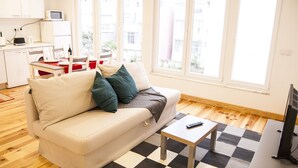 A modern living room with a sofa, a coffee table, and a TV. There is a kitchen area with a microwave and a sink. - Apartamento / Estudio no Centro de Lisboa Para Casal ou Família (Lisboa)