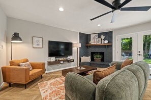 Ein modernes Wohnzimmer mit Flachbildfernseher, Kamin, Deckenventilator und einer Tür zu einem Garten.