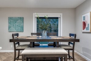 A dining area with a dark wooden table, four chairs, and a bench. There is a vase with branches on the table, and artwork on the walls. - Pecan Grove: Stroll Downtown Frisco (Frisco)