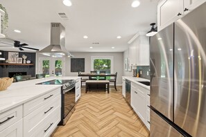 Une cuisine moderne avec des meubles blancs, un réfrigérateur en acier inoxydable et un parquet en bois disposé en chevrons.