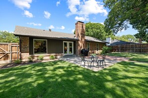 A residential property with a brick exterior, a covered patio with outdoor furniture, and a well-maintained lawn.