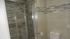 A bathroom with a glass-enclosed shower, a toilet, and tiled walls. - Albergue Roma (Lena)