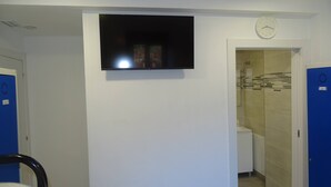 A hotel room with a flat-screen TV mounted on the wall, a clock, and a shower area with a tiled wall. - Albergue Roma (Lena)